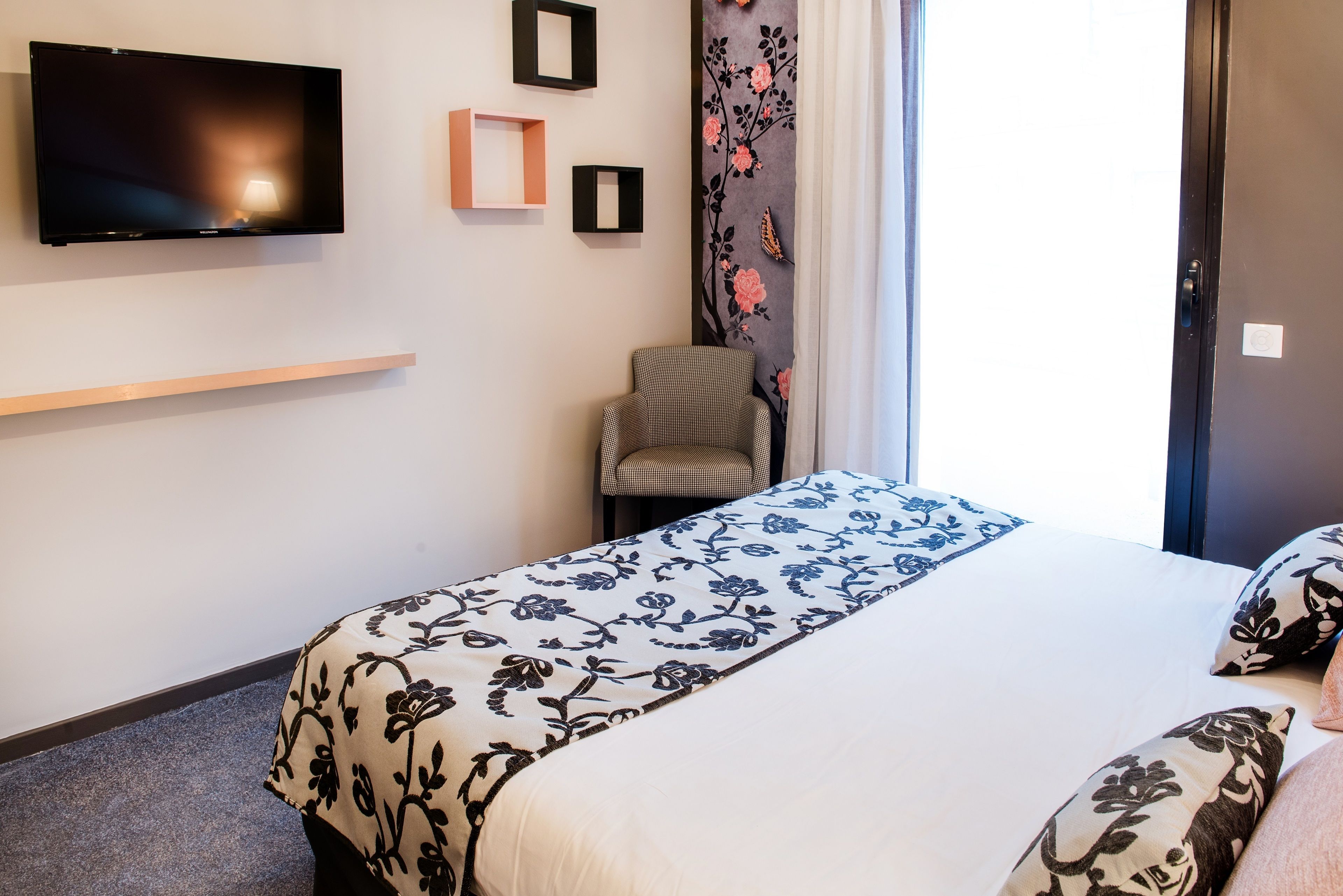 Una habitación de hotel con cama, una silla, un televisor y una ventana con cortinas.