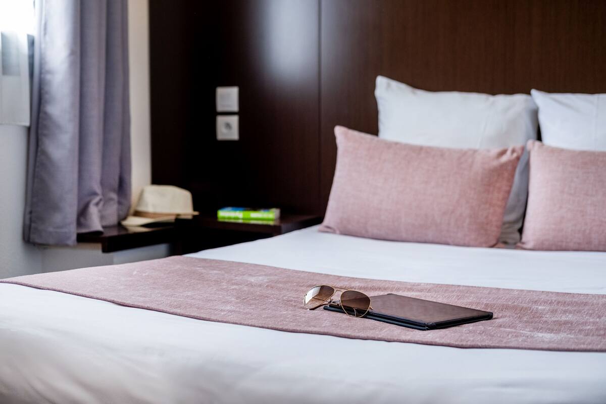 A neatly made bed with a pink blanket, a pair of glasses, and a smartphone on the bed.