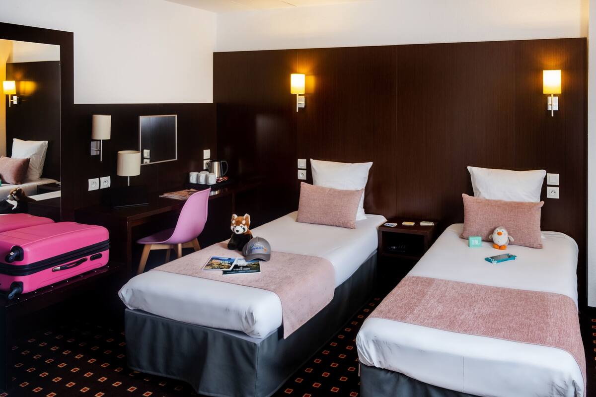 A hotel room with two beds, a desk, a chair, a mirror, and a pink suitcase.