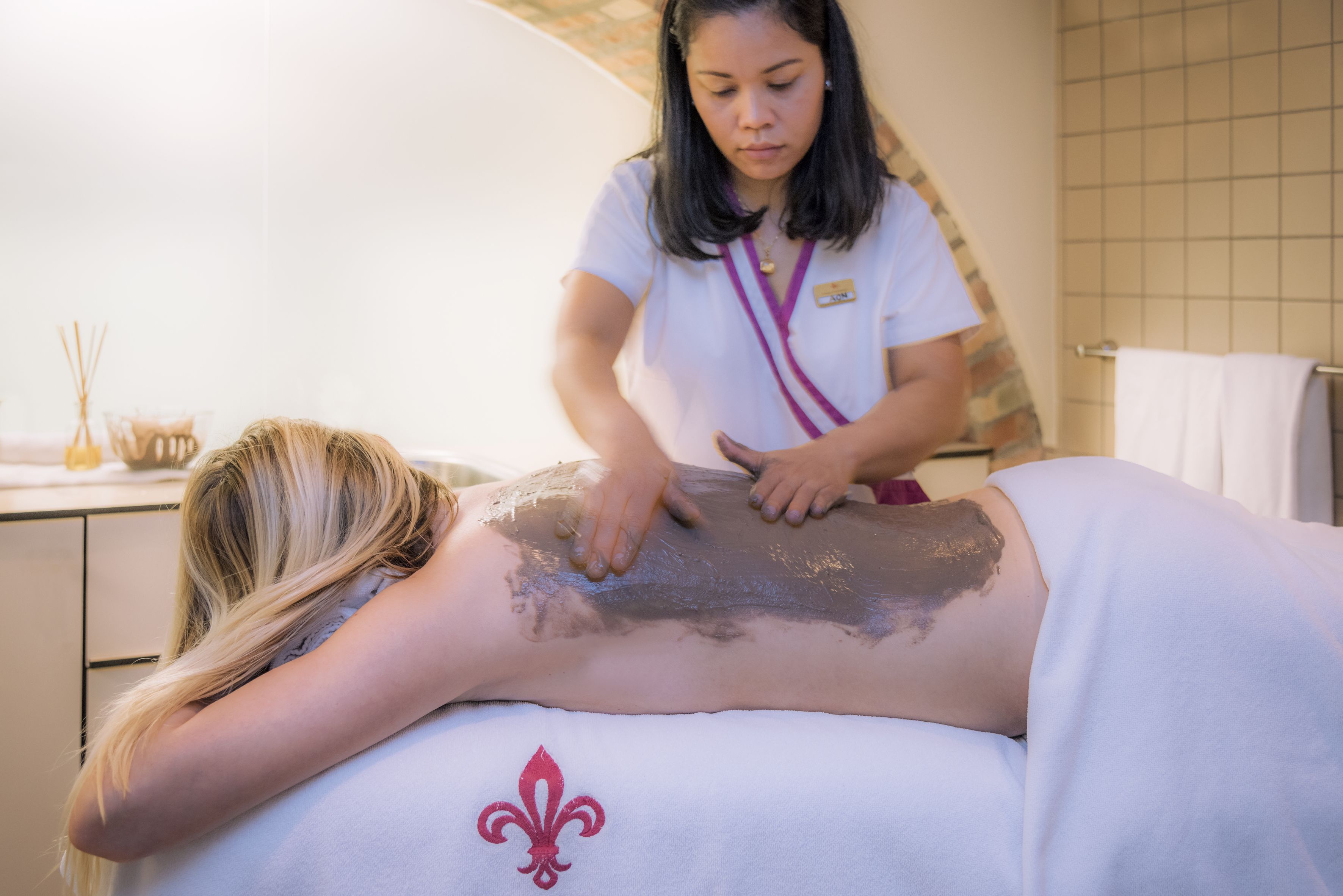A person receiving a massage in a room with a tiled wall and a towel rack.