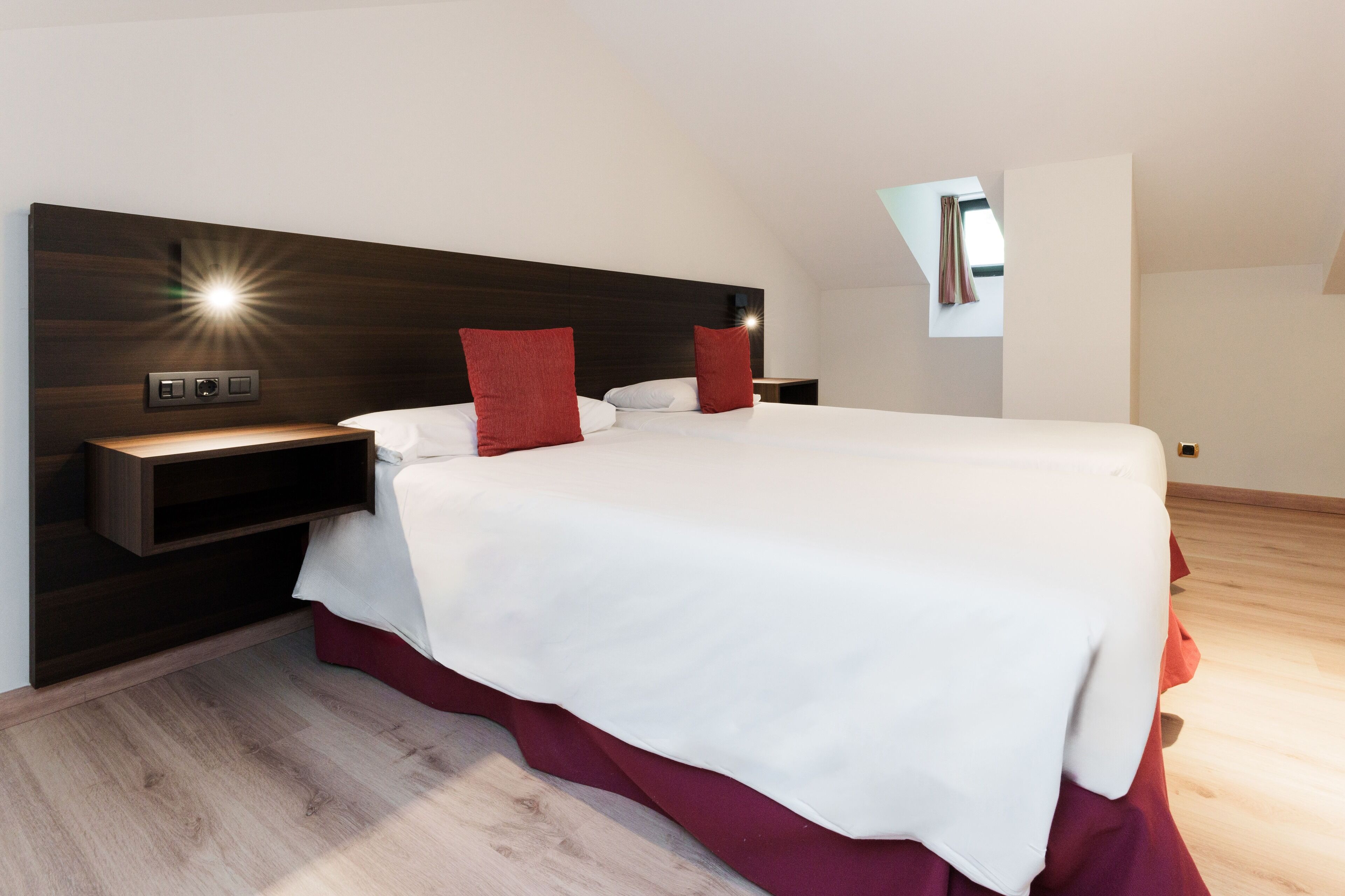 Ein modernes Schlafzimmer mit einem großen Bett, einem Holz-Kopfteil, Nachttischen und einem kleinen Fenster.