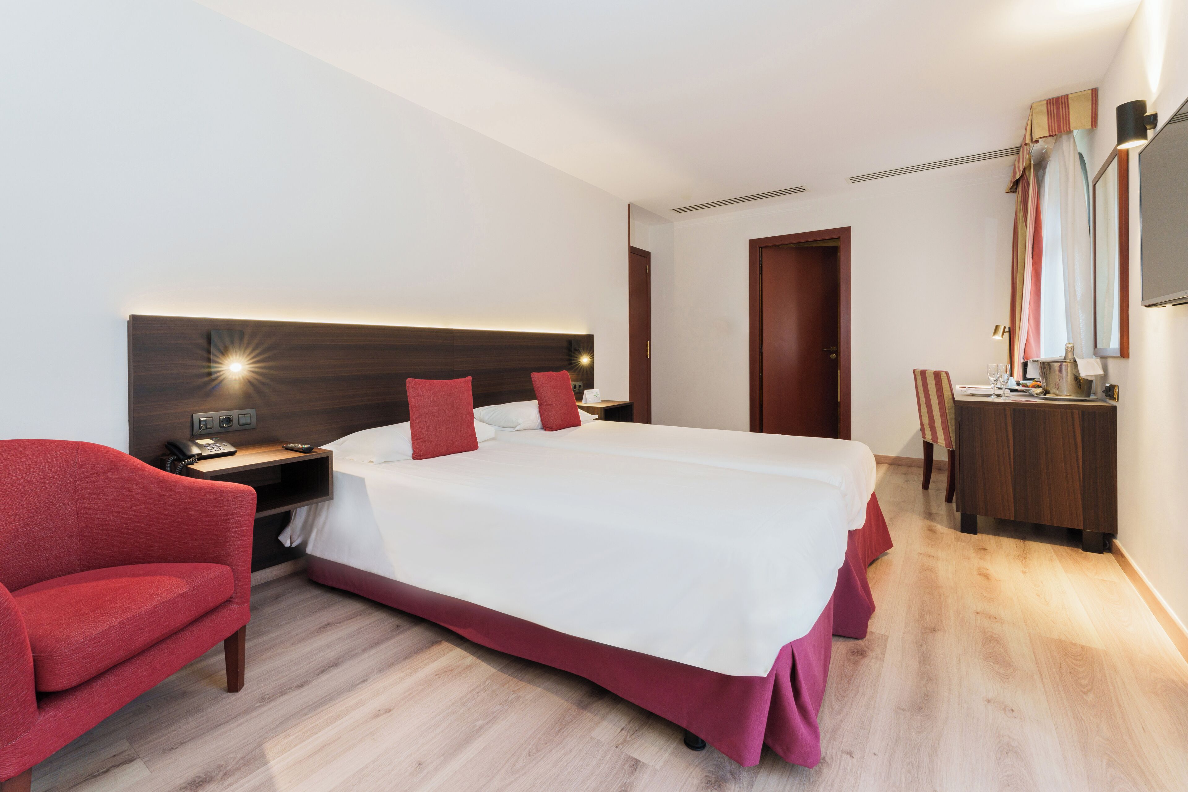 Habitación de hotel con una cama grande, un escritorio con silla, una tocador con espejo y un televisor.