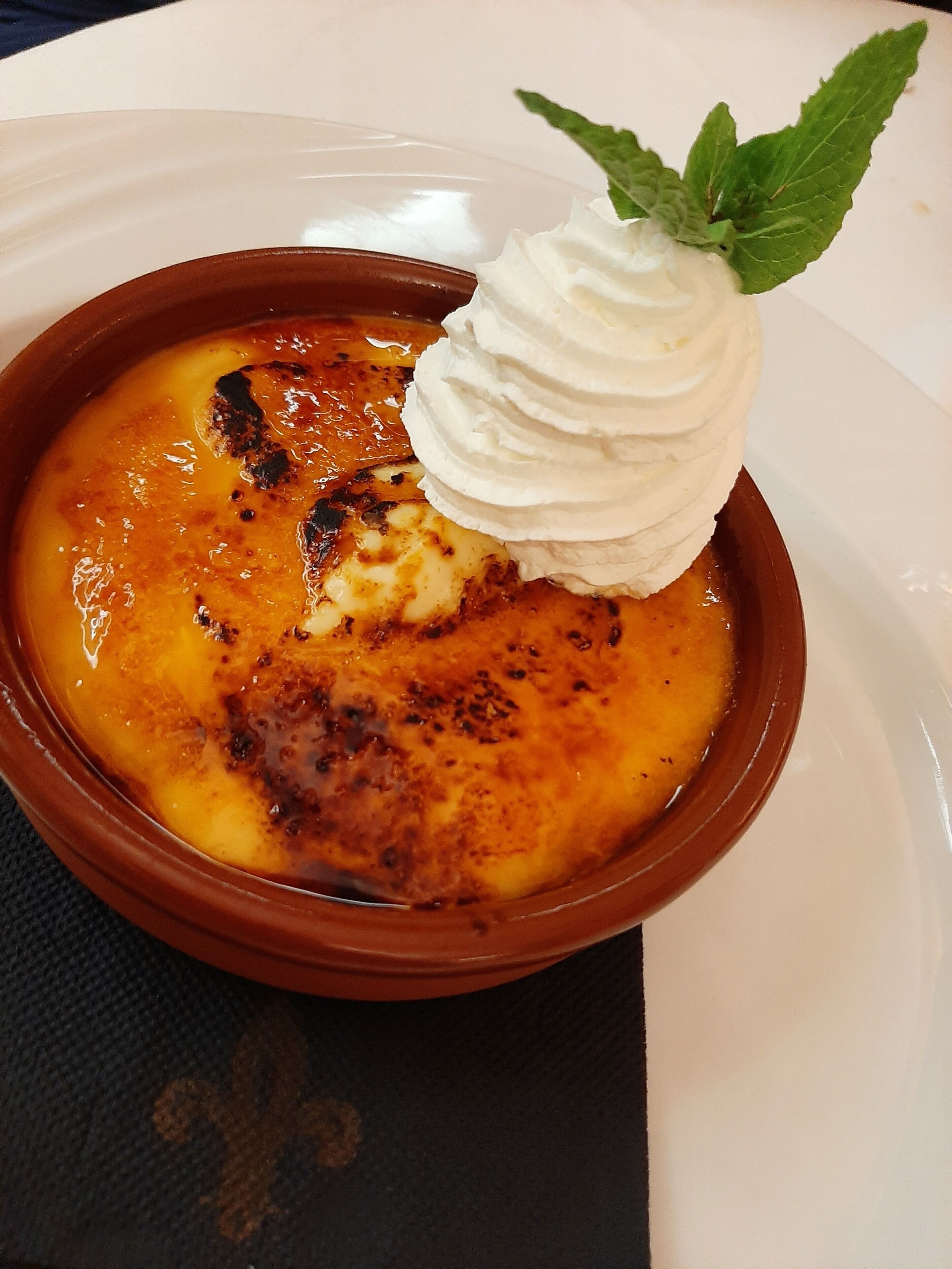 A dessert in a brown bowl with a dollop of whipped cream and a mint leaf on top.