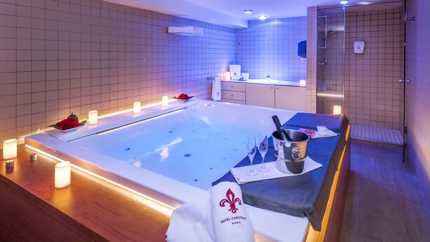 Un spa moderno con una bañera grande, velas, una toalla y una bandeja con una copa de vino y un cubo.