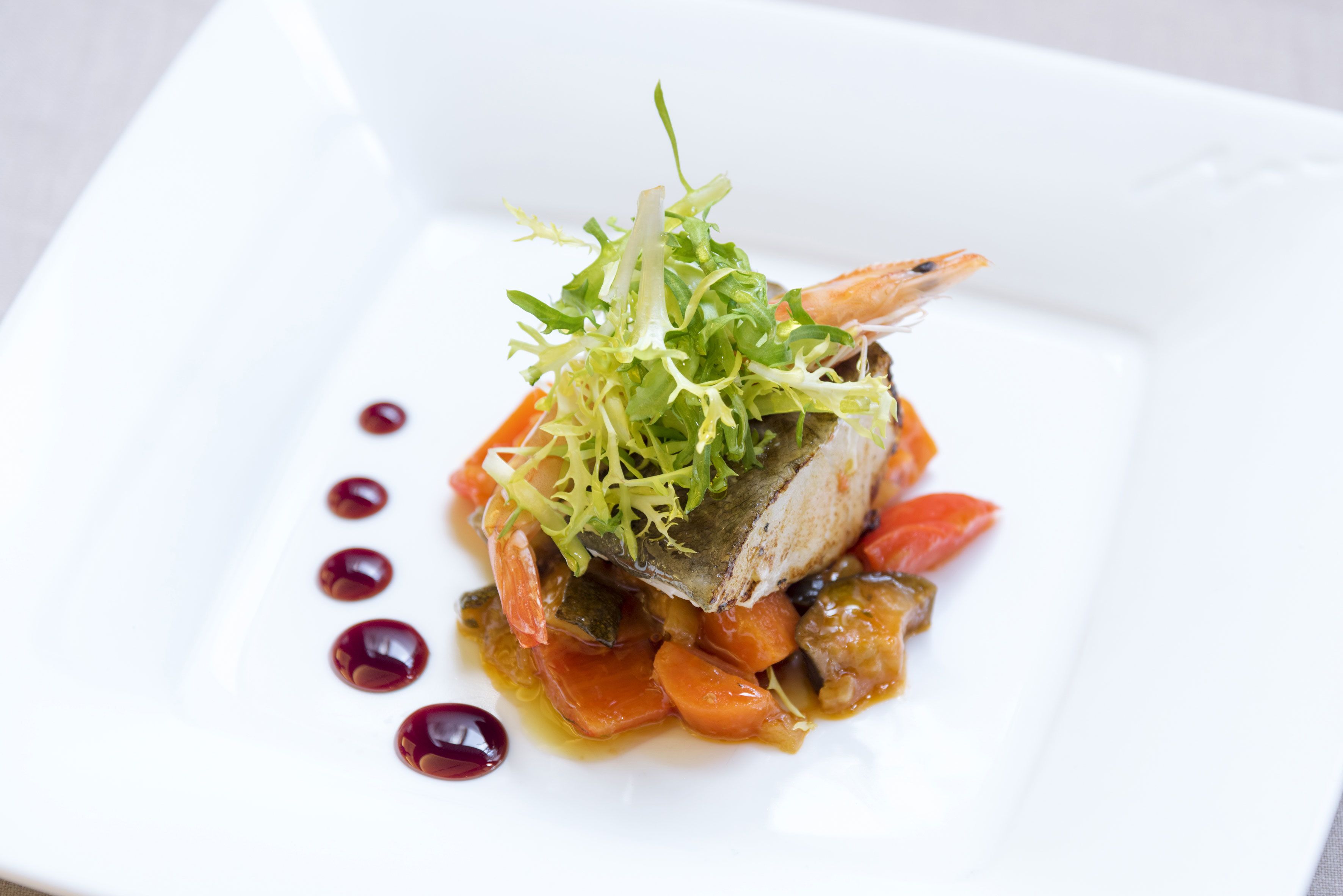 Un plato blanco con un guiso de pescado, verduras y una guarnición.