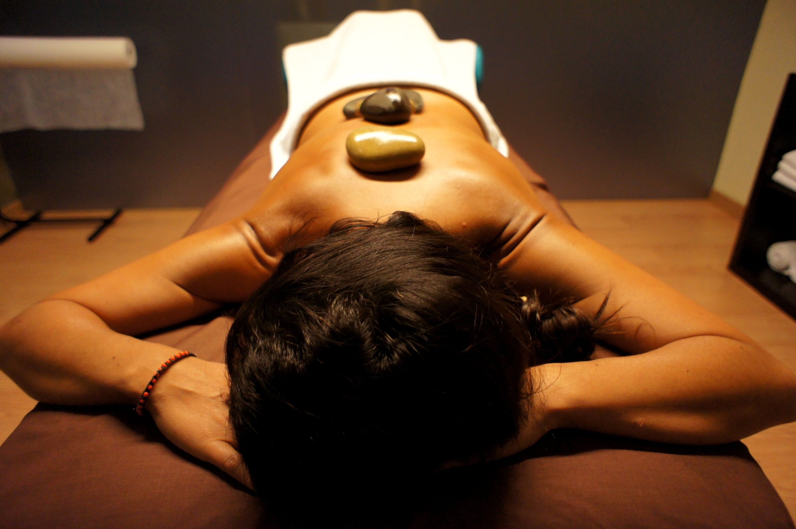 A person lying face down on a massage table with a stone placed on their back.