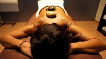 A person lying face down on a massage table with a stone placed on their back.