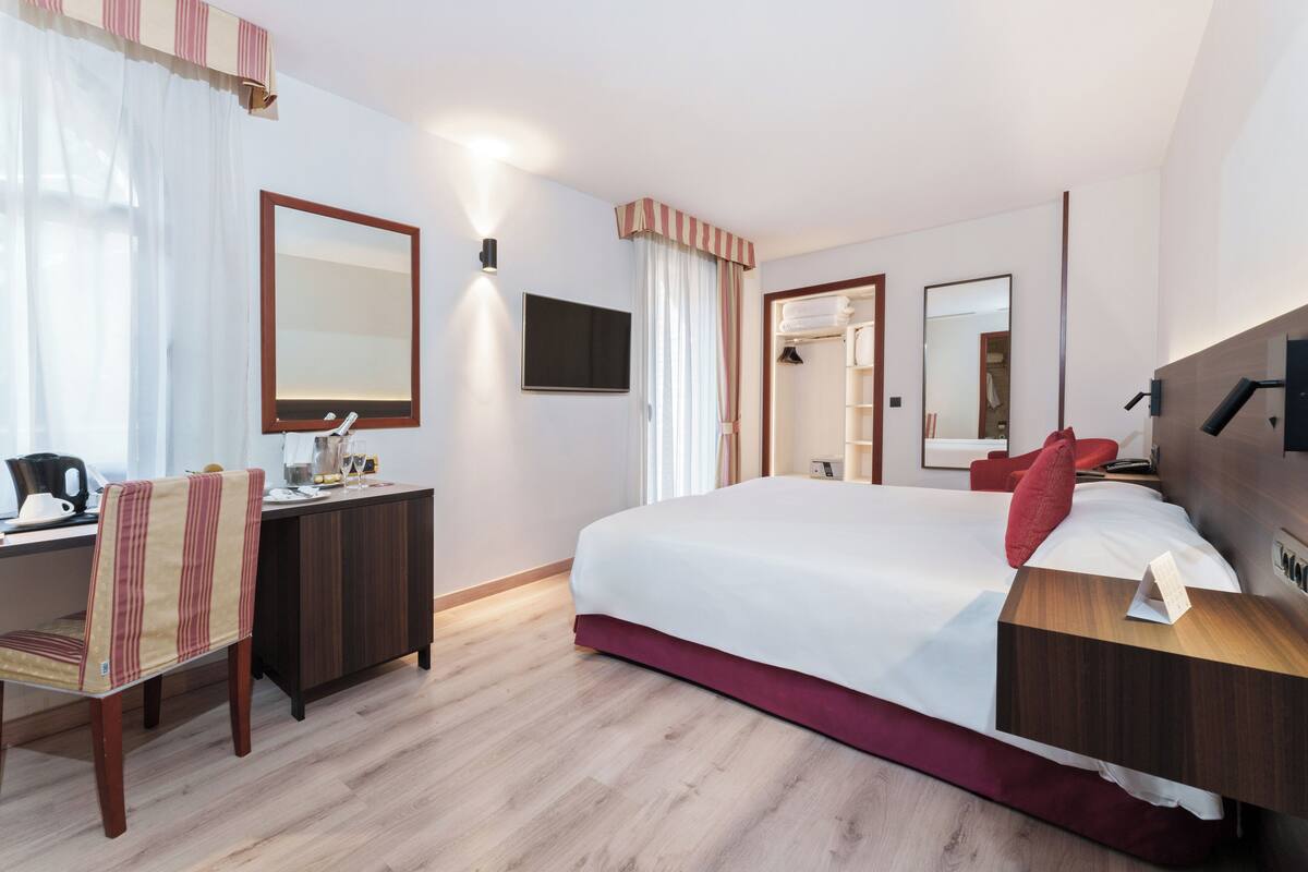 Una habitación de hotel con cama, escritorio, silla, televisor y armario.