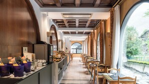 Un amplio comedor con mesas y sillas, una barra de buffet con alimentos y bebidas, y vistas a zonas verdes al exterior.