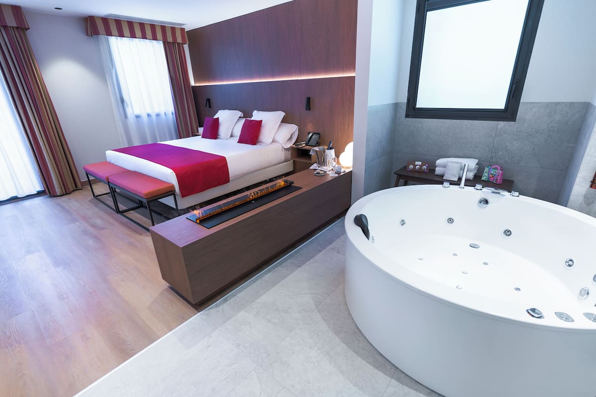 Una habitación de hotel moderna con una cama grande, una zona de estar, una bañera amplia y vistas a la ciudad.