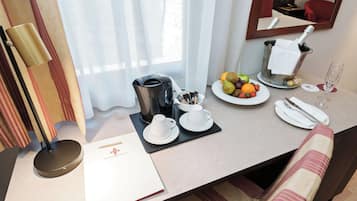 Habitación de hotel con una mesa de desayuno ordenada, que incluye una cafetera, tazas de té, fruta y una copa de vino.