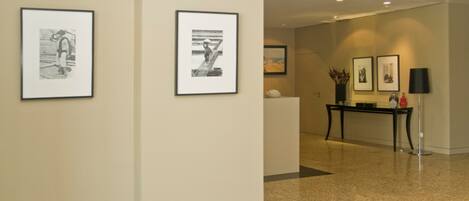 A hallway with framed artwork on the walls, a reception desk, and a lamp.