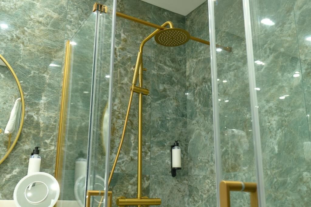 Une salle de bain moderne avec une douche à parois de verre, des murs en marbre et des accessoires dorés.