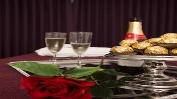 A table with a silver tray holding chocolates, two glasses of champagne, and a red rose.