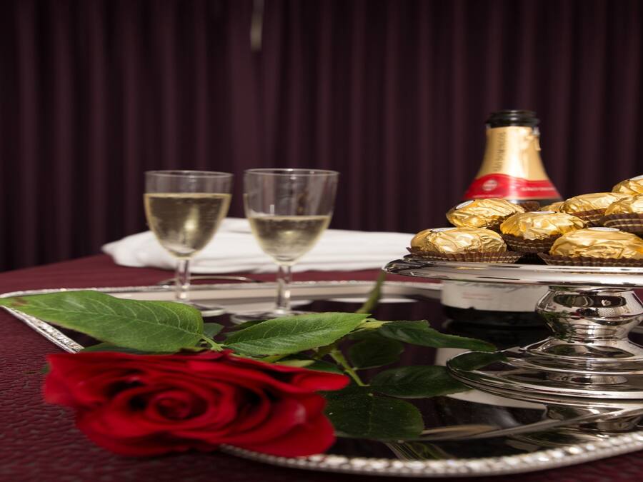 A table with a silver tray holding chocolates, two glasses of champagne, and a red rose.