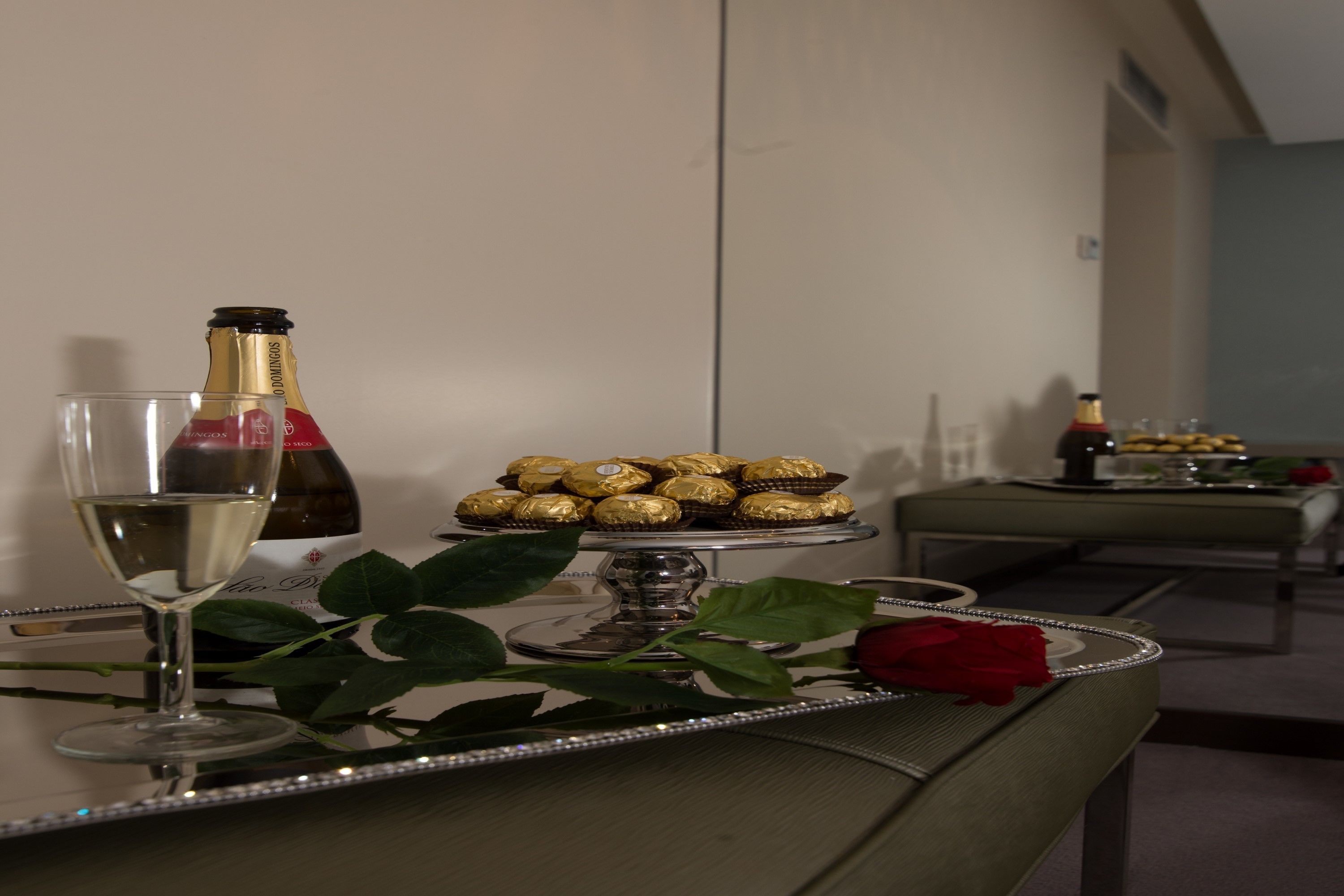 A table with a bottle of champagne, a glass of champagne, and a tray of chocolates.