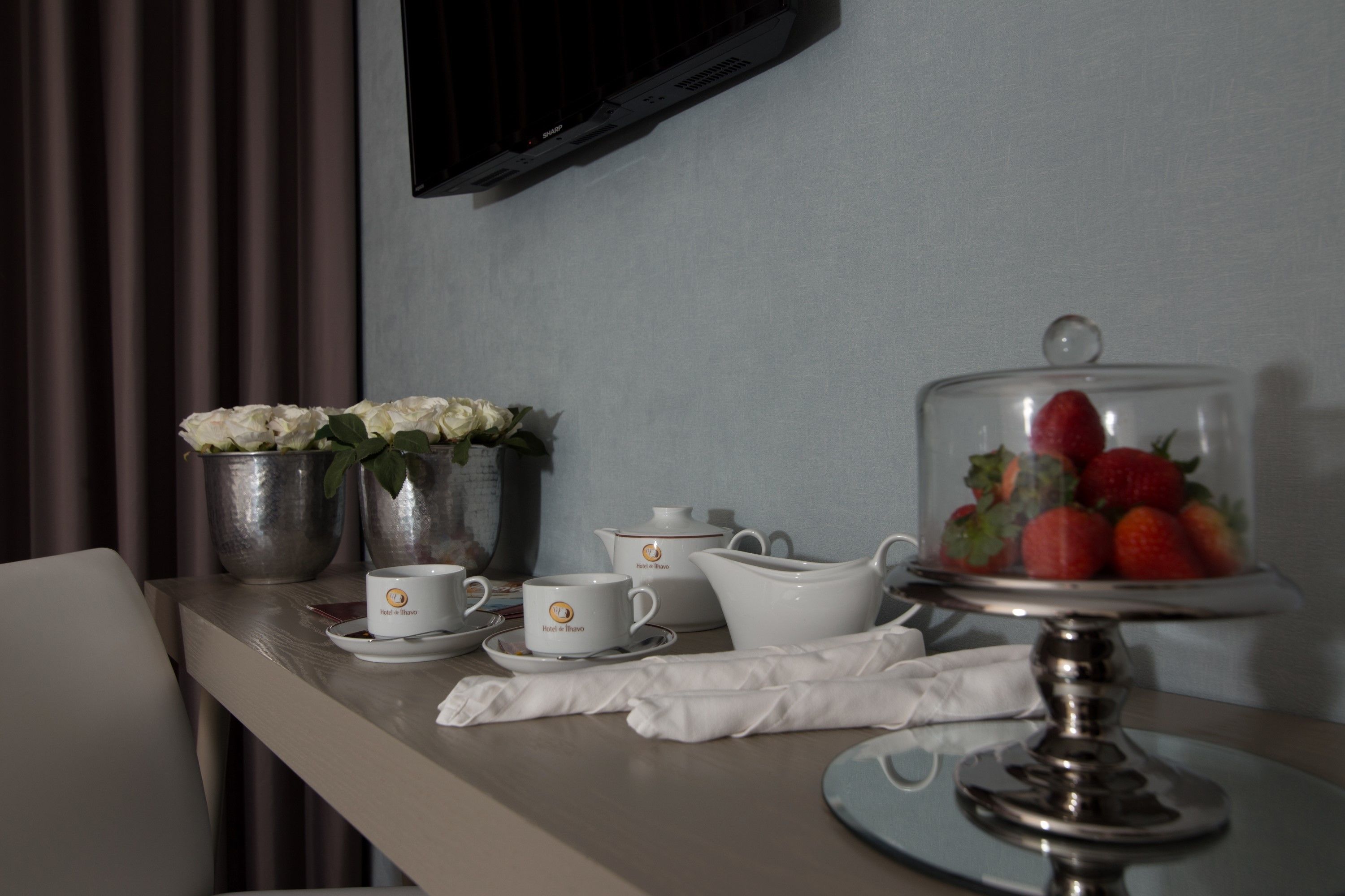 Ein Hotelzimmer mit Esstisch, gedeckt mit weißen Teekannen, Tassen und einer Obstauslage.