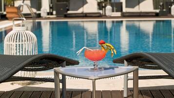 A poolside area with lounge chairs, a table, and a drink with a fruit garnish.