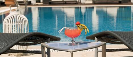 Un espace aménagé au bord de la piscine, avec des chaises longues, une table et une boisson décorée d’un fruit.