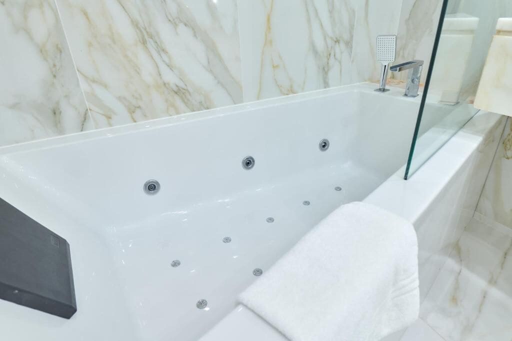 A modern bathroom with a marble wall, a glass-enclosed bathtub, and a white towel.