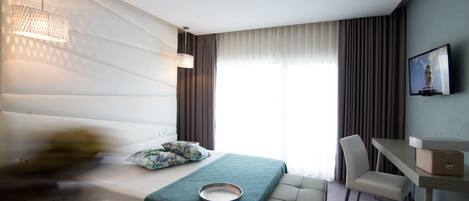 A hotel room with a bed, a desk, a chair, a television, and a window with curtains.
