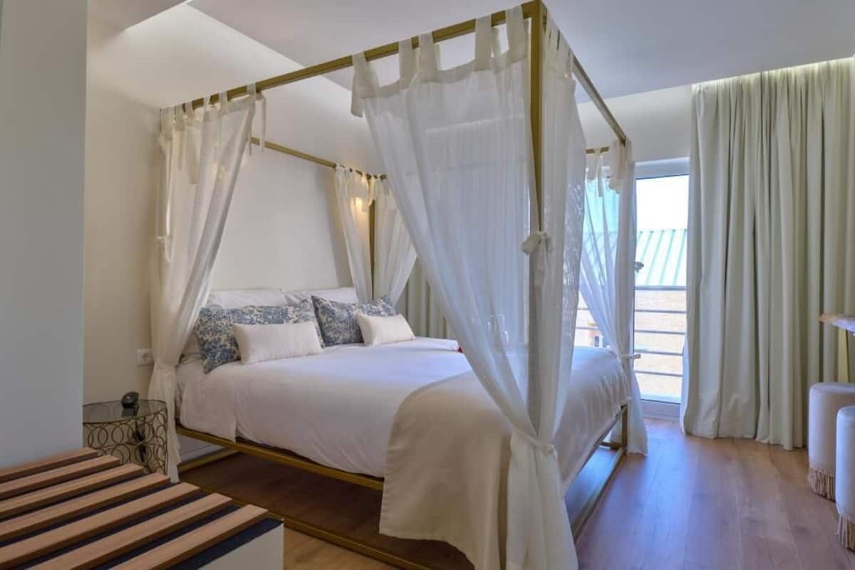 Een hemelbed met witte lakens en blauwe kussens, een glazen salontafel en uitzicht op de omgeving.