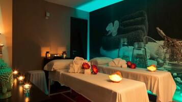 Un cuarto de spa con dos camas, velas y un mural en la pared.