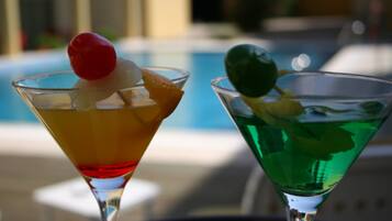 Two cocktails on a table near a pool, with a blurred background suggesting an outdoor setting.