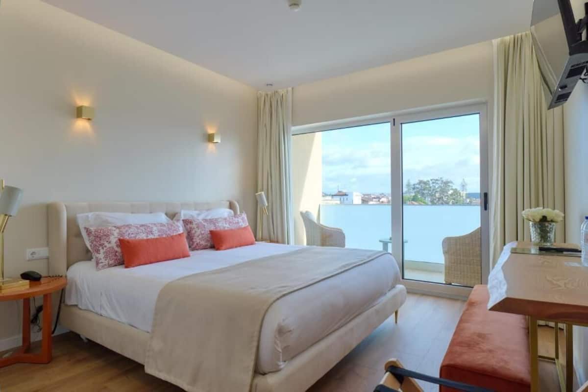 Een hotelkamer met een groot bed, een bureau en uitzicht op het water.