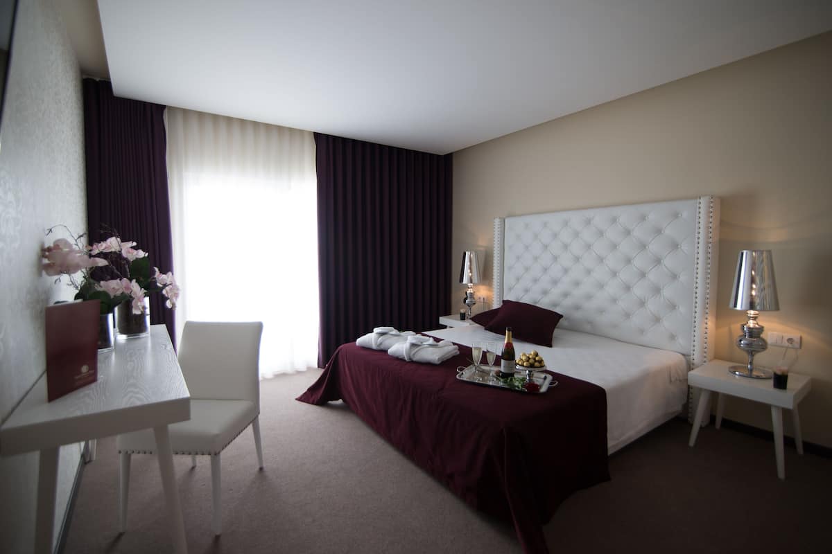 Een hotelkamer met een bed, nachtkastjes, een bureau, een stoel en een raam met gordijnen.