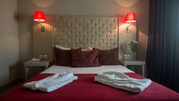 Ein Hotelzimmer mit einer gepolsterten Kopfstütze, roter Bettwäsche, zwei Nachttischlampen, einem Nachttisch mit Telefon und zwei Handtüchern auf dem Bett.