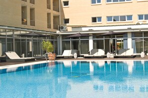 A swimming pool with lounge chairs and umbrellas, surrounded by a building with large windows and balconies.