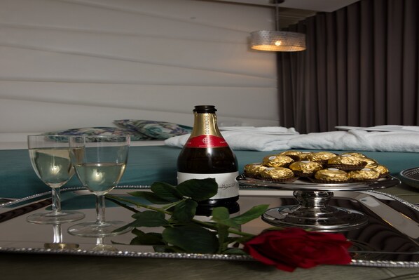 A tray with a bottle of champagne, two glasses, a rose, and chocolates on a table in a hotel room.