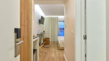Een hotelkamer met een houten garderobe, een klein tafeltje met een stoel, een aan de muur bevestigde televisie, een bed met een witte dekbedovertrek en een raam met gordijnen.