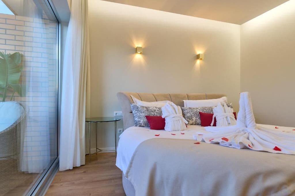 A hotel room with a bed, two wall-mounted lights, a glass partition, and a small table.