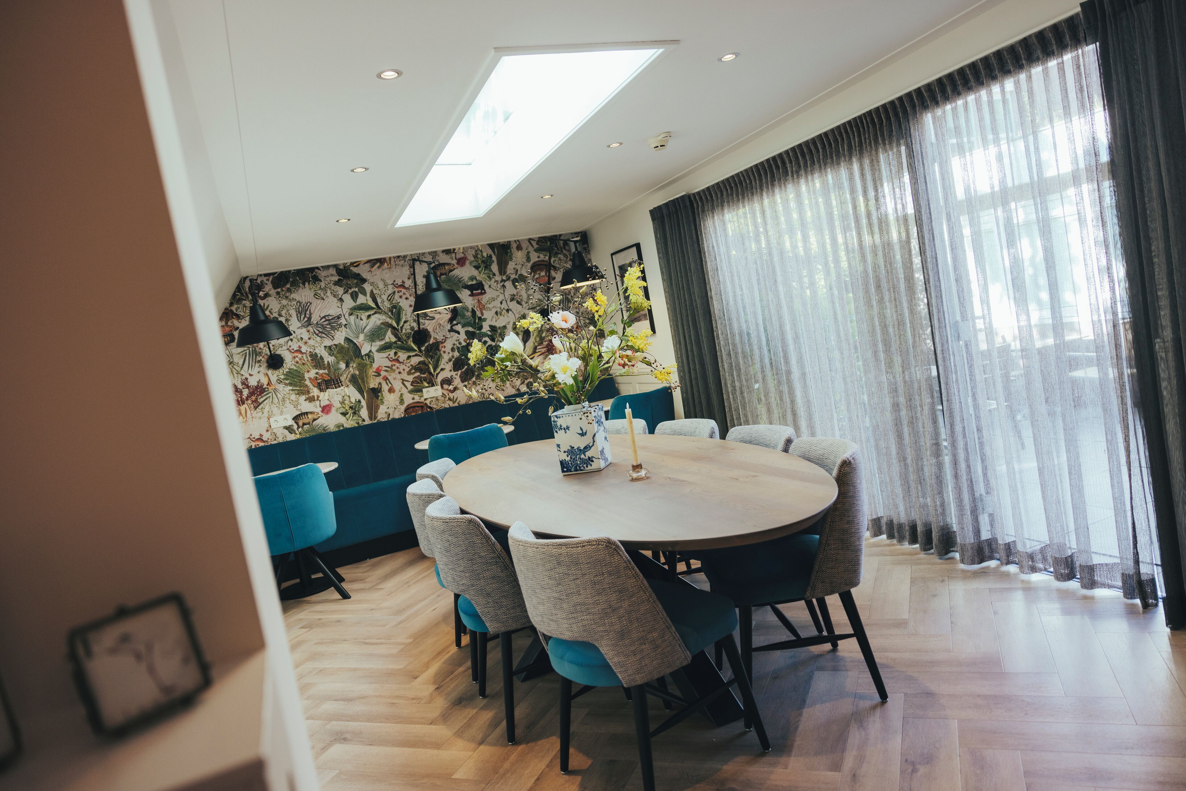 Een eethoek met een ronde tafel, stoelen en een bloemen behang.