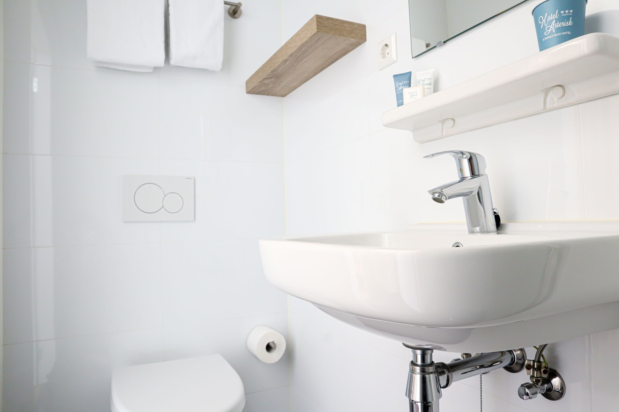 Un baño moderno con un lavamanos blanco, un inodoro y un estante de madera sobre el lavamanos.