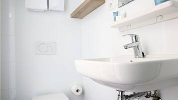 Un baño moderno con un lavamanos blanco, un inodoro y un estante de madera sobre el lavamanos.