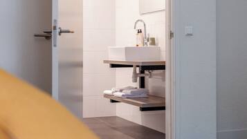 Habitación de hotel con cama, baño con lavamanos y espejo, y puerta que da a otra habitación.