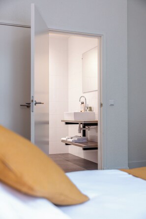 A hotel room with a bed, a bathroom with a sink and mirror, and a door leading to another room. - Boutique Hotel Asterisk, a family run hotel (Amsterdam)