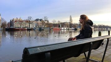 A person sitting on a bench by a calm river with buildings in the background.