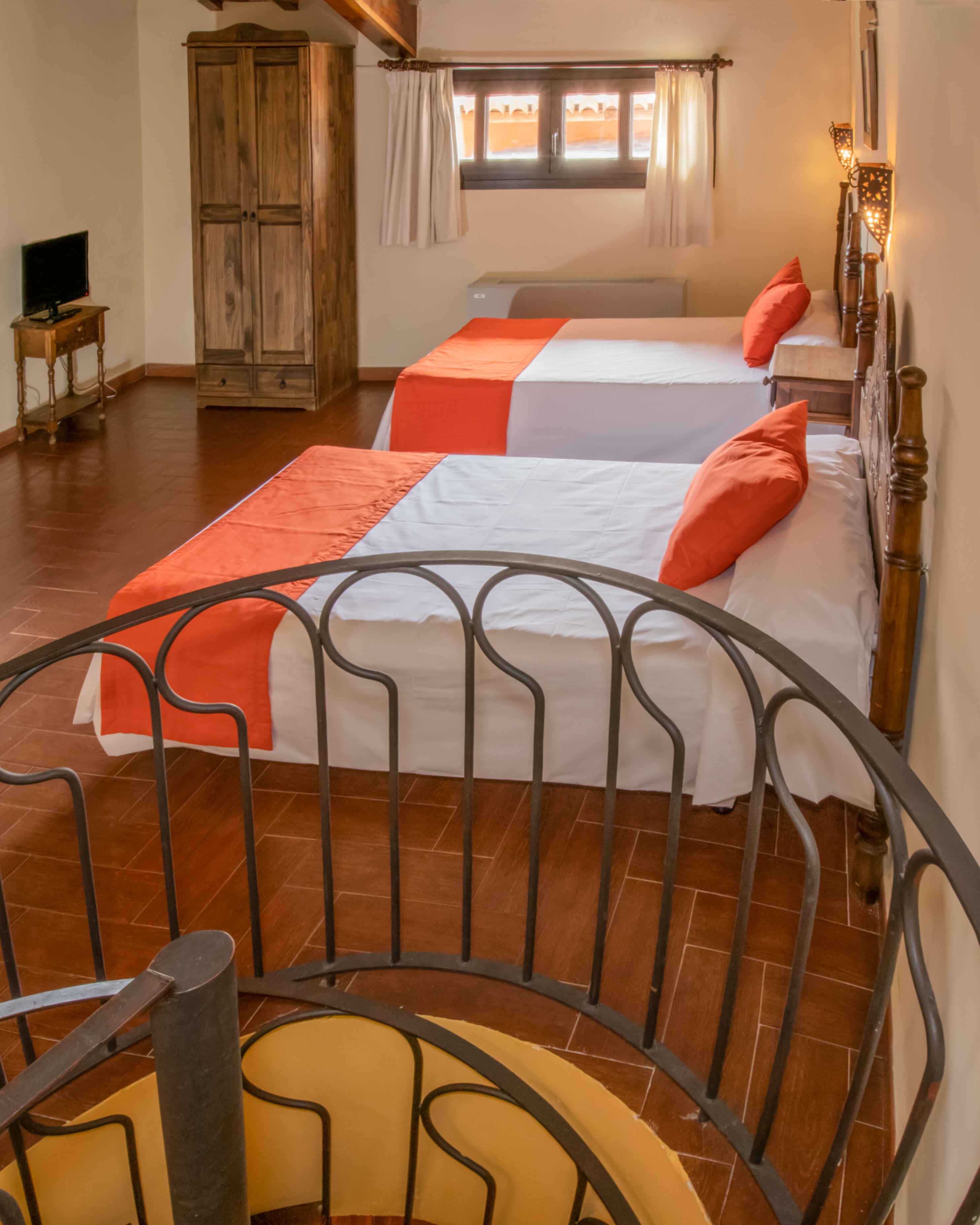 Una habitación con dos camas, un armario de madera, un televisor y una escalera.