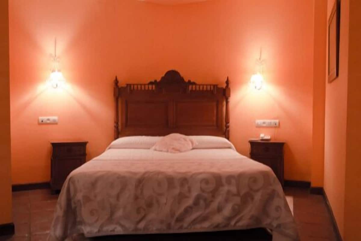 A bedroom with a wooden bed, two bedside tables, and wall-mounted lights.