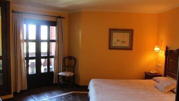A hotel room with a bed, a chair, a window with curtains, a framed picture on the wall, and a nightstand with a lamp.