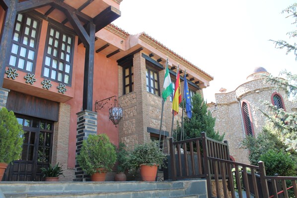 Un bâtiment doté d’une façade en pierre, de nombreuses fenêtres et d’un mât sur lequel flottent différents drapeaux.