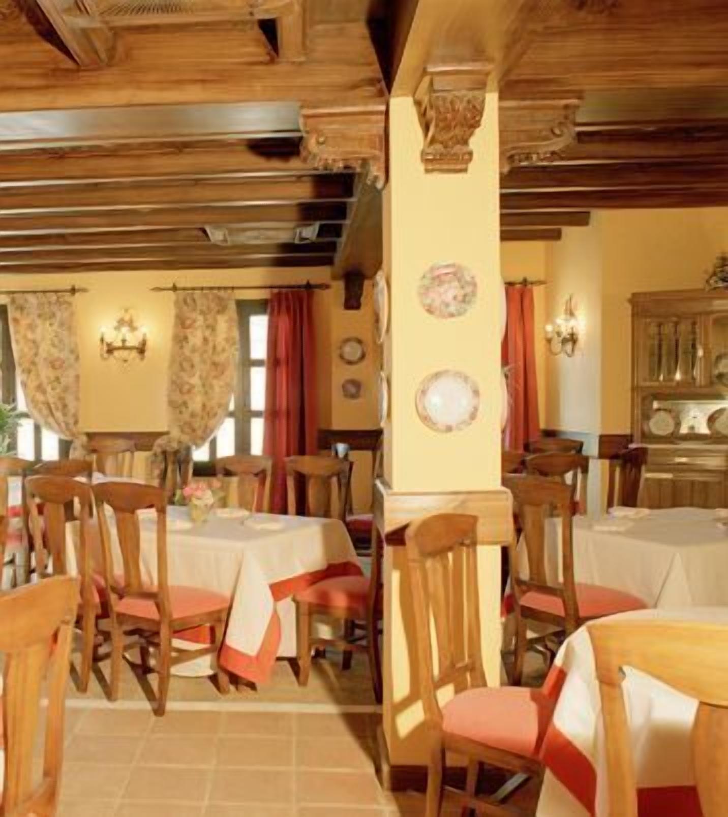 A dining area with wooden tables and chairs, a chandelier, and a wall with decorative plates.
