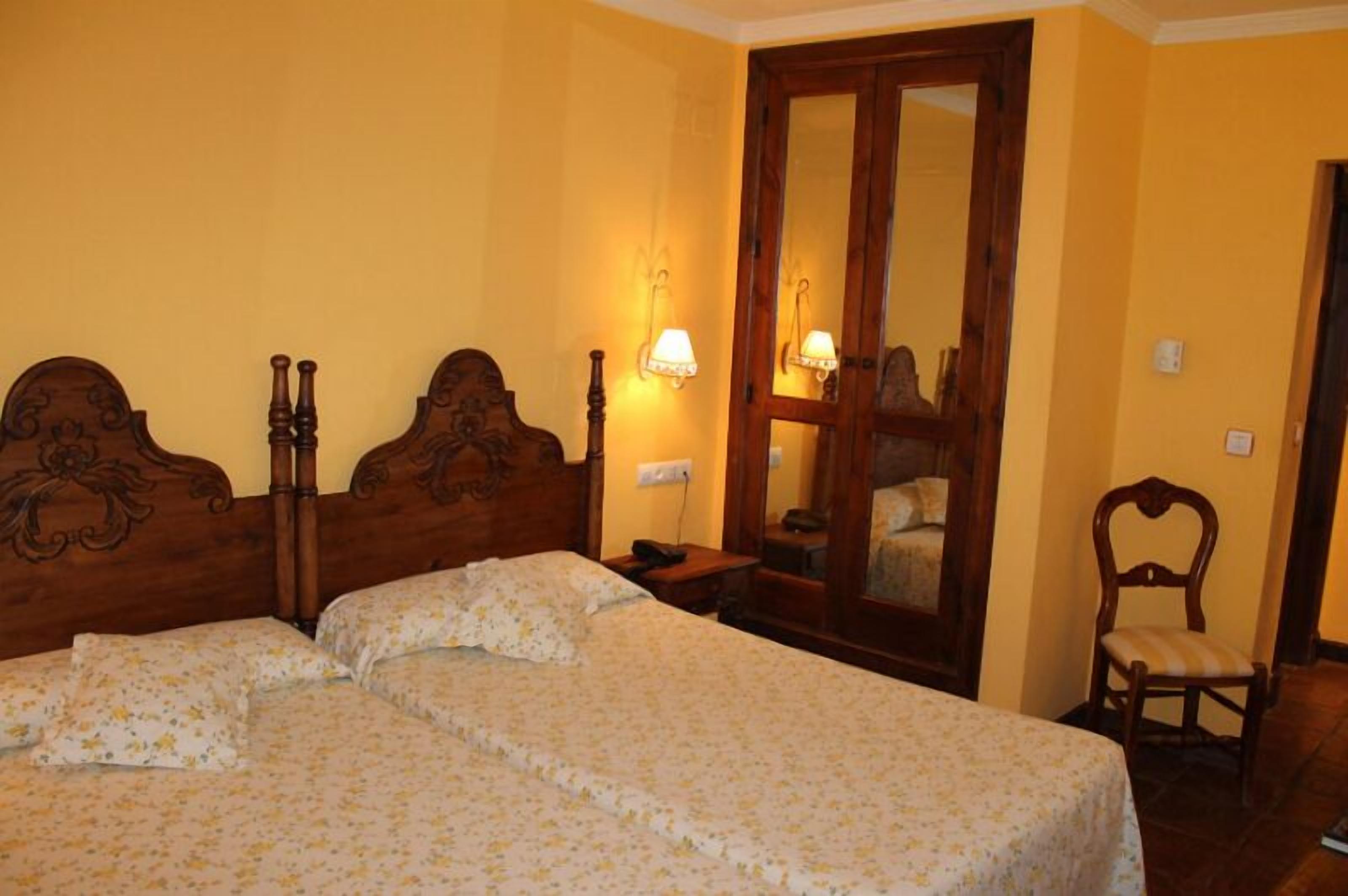 A room with a double bed, two bedside tables, a chair, and a mirror.