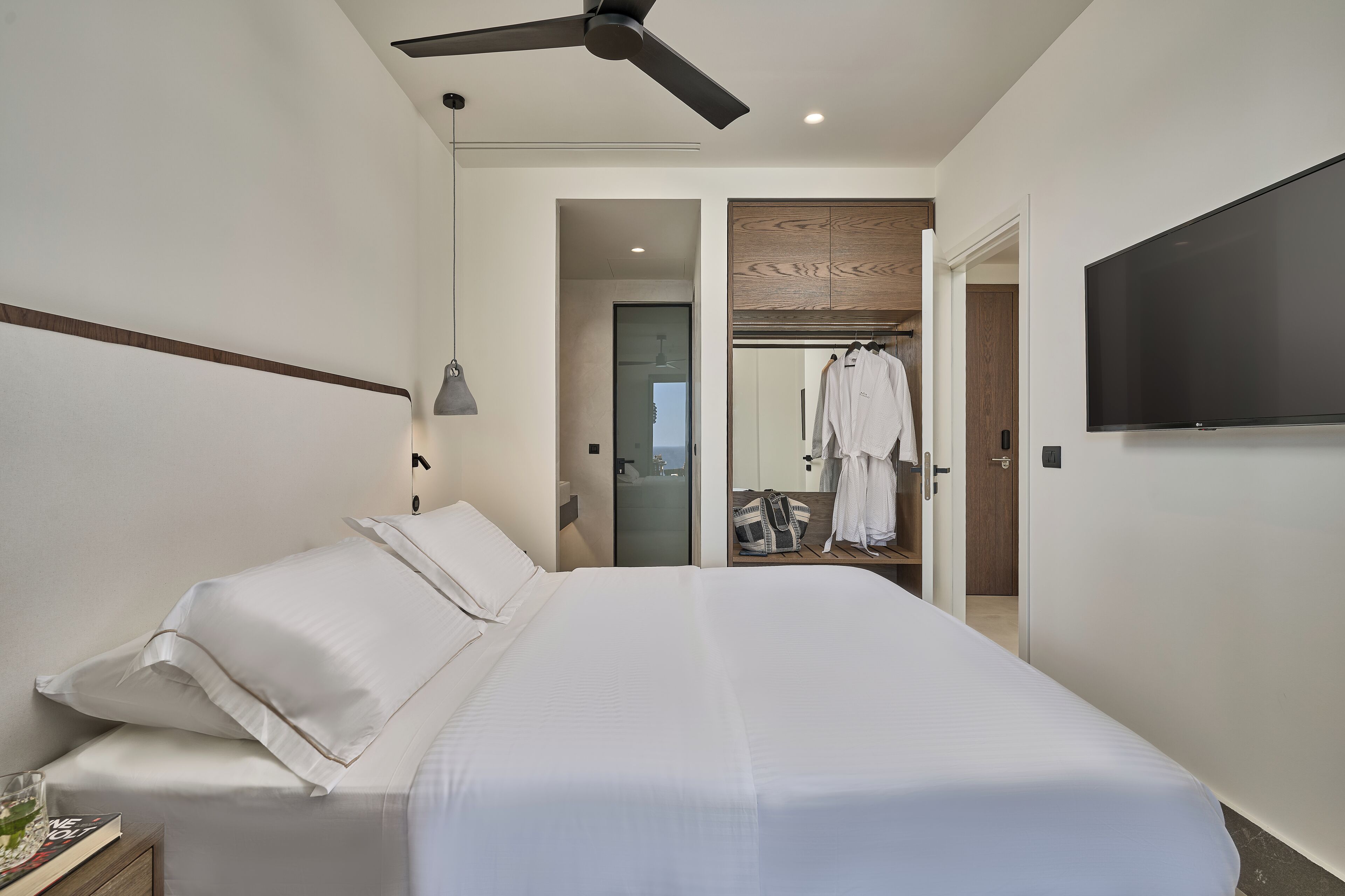 A modern hotel room with a large bed, a ceiling fan, a flat-screen TV, and a walk-in closet.
