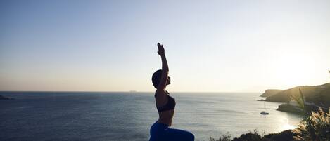 A person performing a yoga pose on a mat with a scenic ocean view in the background.