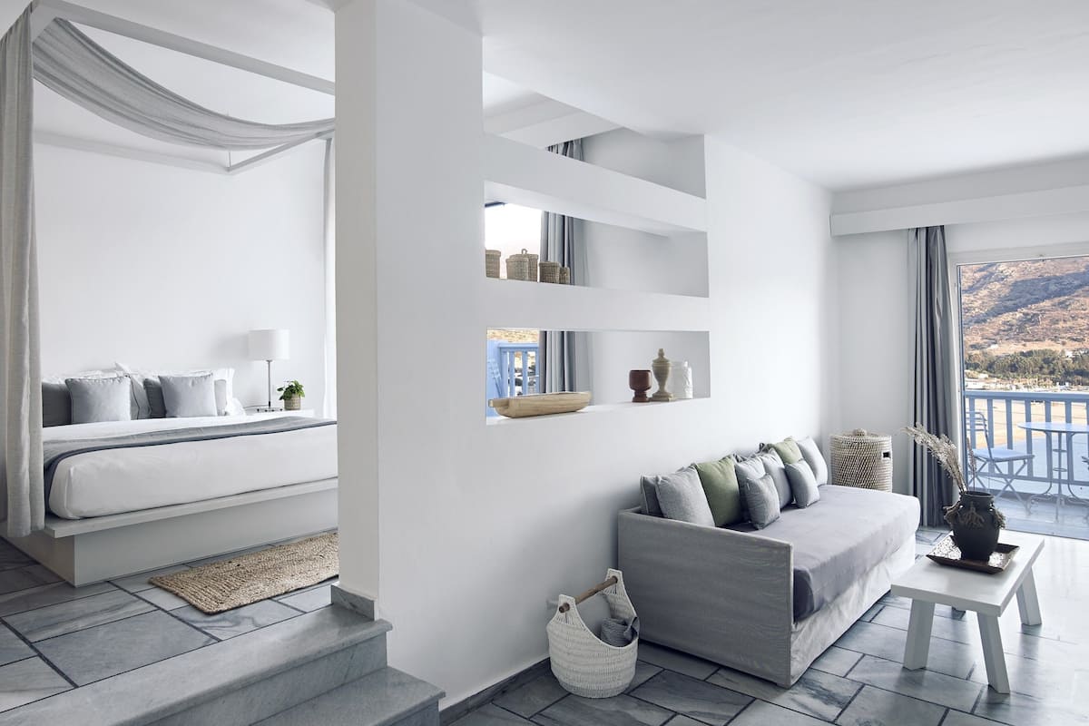 A modern hotel room with a balcony, a sofa, a small table, and a bed with curtains.